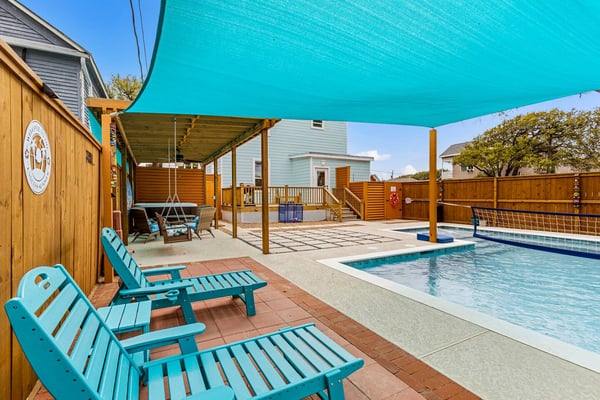 Backyard with swimming pool, turquoise shade sail, wooden pergola, lounge chairs, and houses with wooden fencing