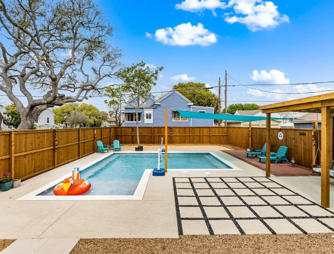 Backyard with rectangular swimming pool, wooden fence, turquoise lounge chairs, and large oak tree